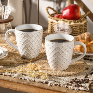 Two patterned mugs with coffee on a rustic table setting with a basket and bread.