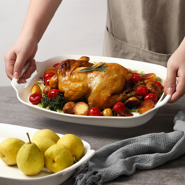 Roasted chicken with vegetables on serving platter with handles, held by a person.