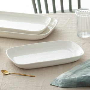 Set of white ceramic trays on a table with a glass and gold spoon.