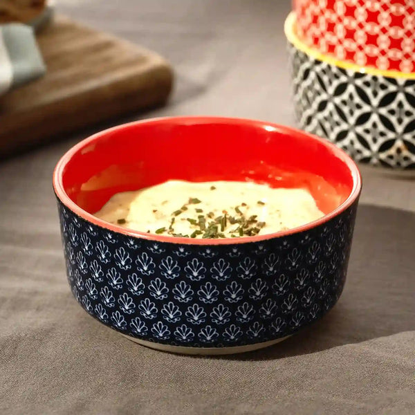 Ceramic dipping bowl with red interior and black exterior pattern on a gray surface