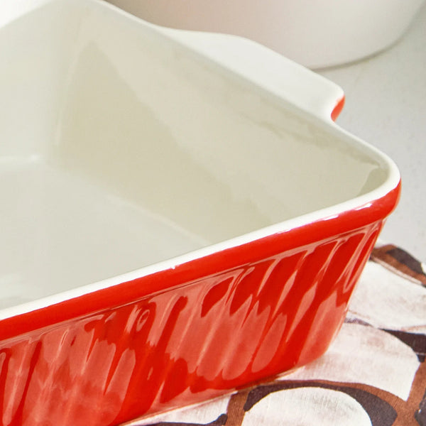 Rectangular ceramic baking dish with red exterior and white interior on a patterned surface