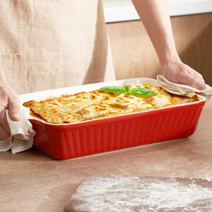 Person holding a red baking dish with lasagna on a wooden surface