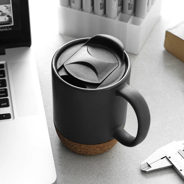 ceramic coffee mug with lid on a desk next to a laptop