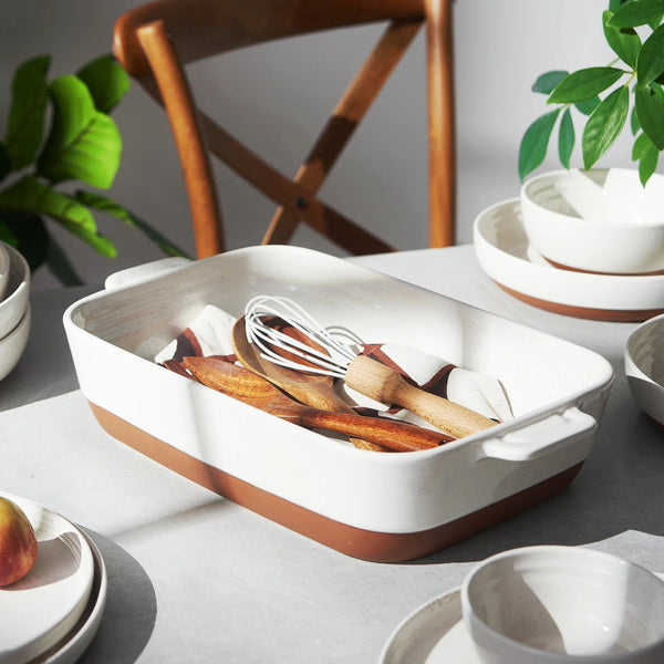 Rectangular baking dish with kitchen utensils on a table with plants in the background