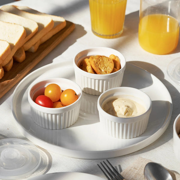 Breakfast setting with toast, orange juice, and small ramekins of food on a white surface.