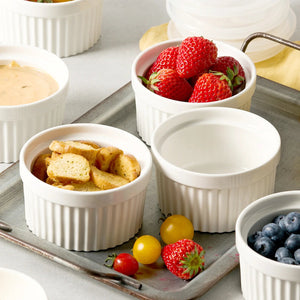 Set of white ramekins with various food items including berries and bread on a tray.