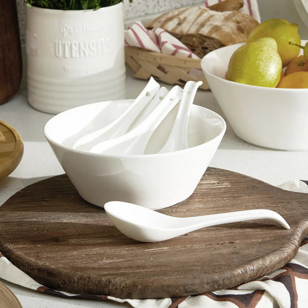 White ceramic spoons on a wooden cutting board with a bowl of pears in the background.
