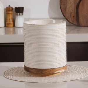 White ribbed ceramic vase with wooden base on a white surface