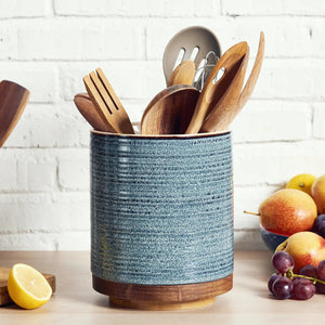 Blue textured kitchen utensil holder with wooden utensils on a white brick wall background.