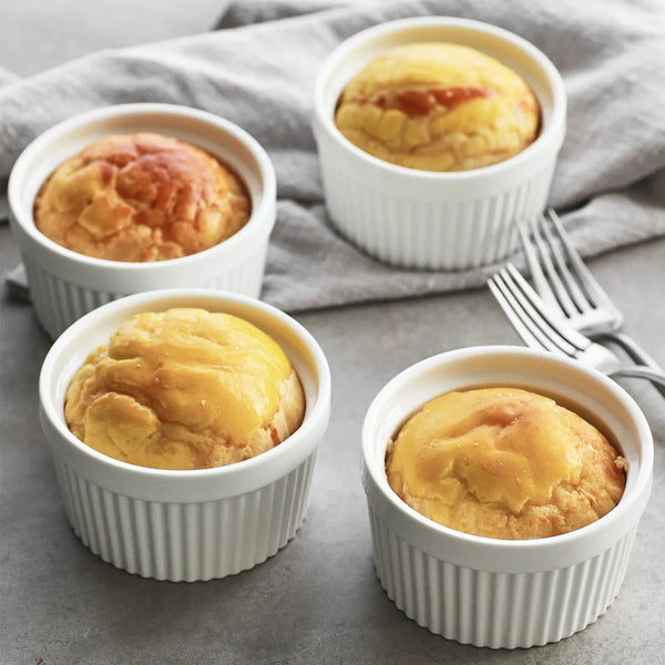 Four small baked goods in white ramekins on a gray surface with a fork.