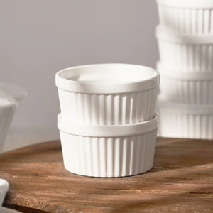 Two white ceramic ramekins stacked on a wooden surface with a neutral background
