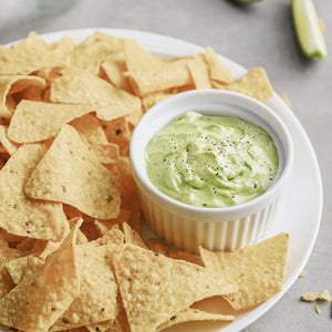 Tortilla chips with a bowl of green dip on a white plate