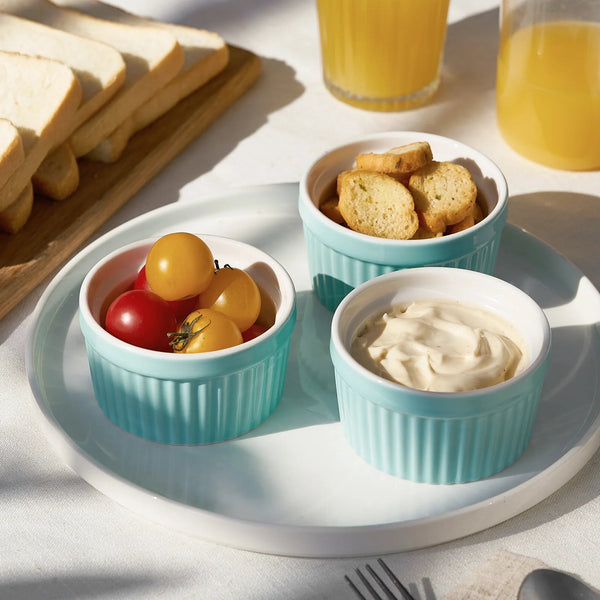 Three turquoise ramekins on a white plate with tomatoes, crackers, and cream cheese.