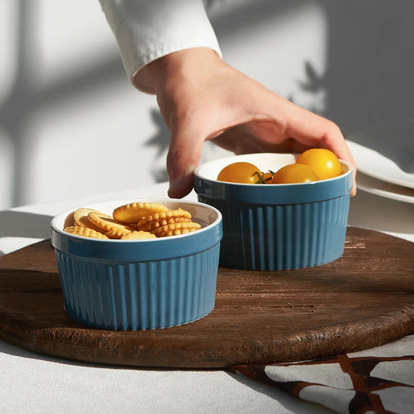 Two blue ramekins on a wooden surface with a hand reaching for one of them.