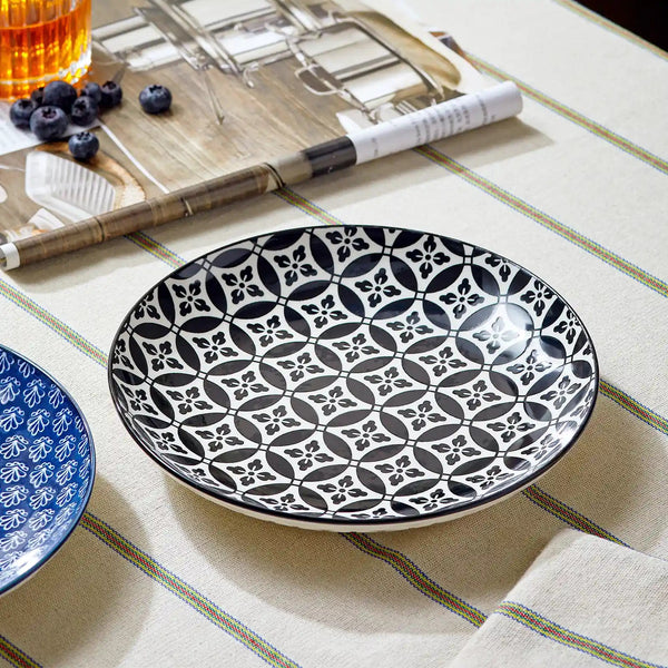 Ceramic plate with black geometric pattern on a table with a glass of tea and blueberries.