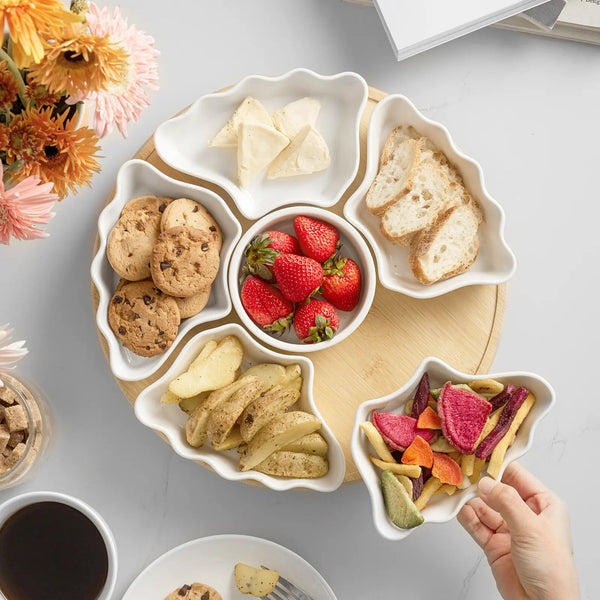 Round white plate with various snacks including cookies, fruit, and crackers on a light gray surface.