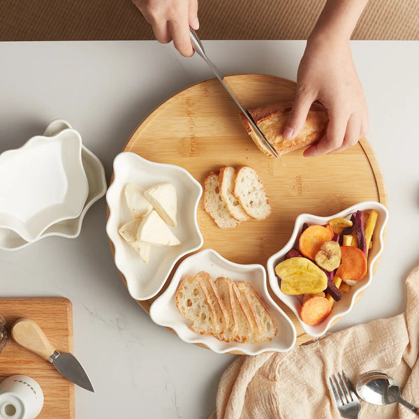 Person slicing bread on a wooden cutting board with various food items around