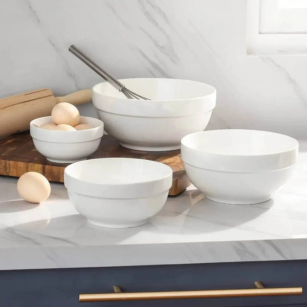 Set of white ceramic bowls on a kitchen counter with a rolling pin and eggs.