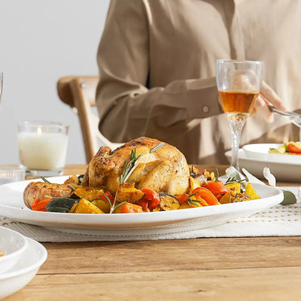 Roasted chicken with vegetables on a plate with a glass of wine and a person in the background.