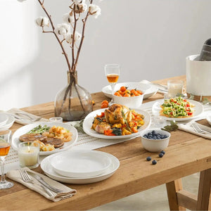 ceramic serving dishes with plates of food, glasses, and a vase with cotton branches.